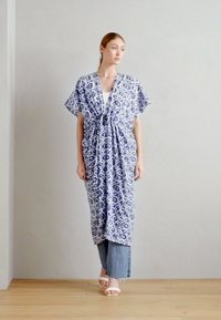 Kimono fluide, de longueur cheville, en tissu à motifs bleu et blanc, avec des manches courtes et une fermeture à nouer, superposé sur un pantalon en denim.
