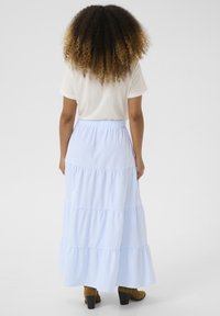 Jupe maxi rayée bleu clair avec un design en étagères, une taille élastique et une silhouette fluide. Complétée par des bottes à talons marron.