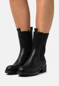 Botines negros de tobillo hechos de cuero suave, con paneles laterales elásticos, un tacón grueso y una suela de goma texturizada para mejorar el agarre.
