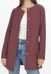 Burgundy lång jacka med rund halsringning, tryckknappar och två sidofickor. Tillverkad av ett slätt, strukturerat tyg.