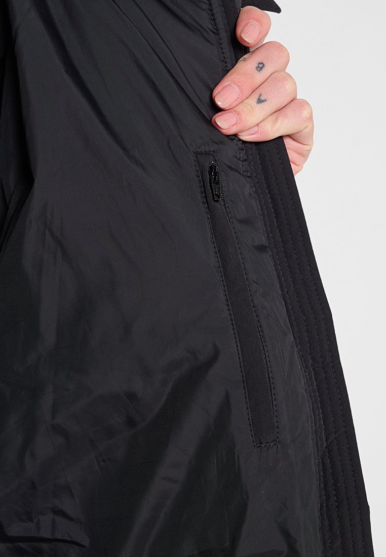 Schwarze, leichte Jacke mit einer Reißverschlusstasche, strukturiertem Stoff und dezenten Nähten entlang der Säume.