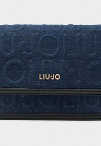 Borsa a tracolla in denim di colore blu scuro con design del logo in rilievo. Presenta una finitura in finta pelle nera e un emblema del marchio in tono oro.