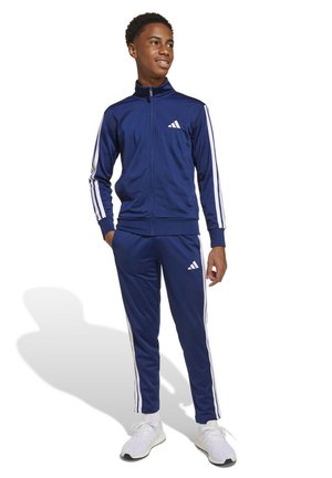 Chándal azul marino de adidas con rayas blancas a lo largo de las mangas y los pantalones. Chaqueta con cremallera, cintura elástica y tejido texturizado.