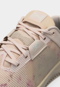 Κοντινό πλάνο αθλητικού παπουτσιού ανοιχτού ροζ χρώματος με ύφασμα από δίχτυ, υφή στη σόλα, κορδόνια και λογότυπο στη γλώσσα και την πλευρά.