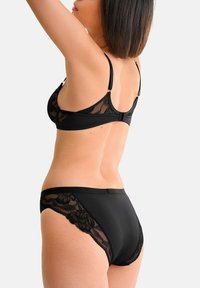 Soutien-gorge noir avec dentelle et culottes taille haute assorties. Détails en dentelle transparente sur le soutien-gorge et les côtés des culottes. Texture de tissu lisse.