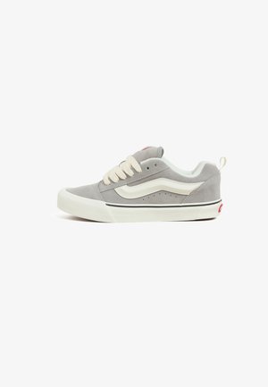 Gray suede low-top sneaker with cream laces, white side stripe, and black accents, featuring perforations for breathability and a rubber sole.
