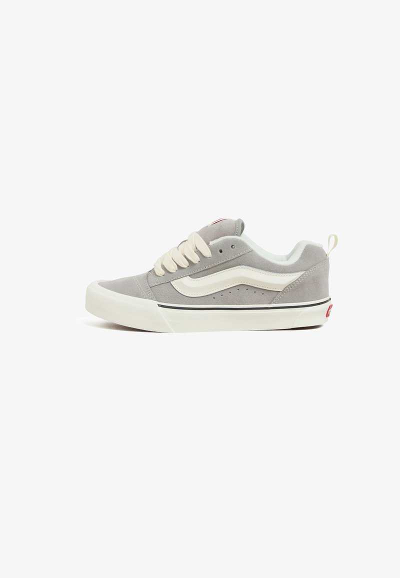 Gray suede low-top sneaker with cream laces, white side stripe, and black accents, featuring perforations for breathability and a rubber sole.