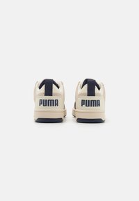 Paire de baskets Puma beige vues de dos, avec des languettes bleu marine et le logo Puma sur les contreforts du talon.