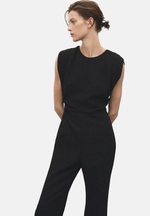 Combinaison noire à manches courtes, avec un corsage ajusté et des jambes fuselées. Fabriquée en tissu texturé, elle présente des lignes épurées et un design minimaliste.