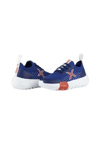 Zapatillas deportivas azules con un upper de malla texturizada, suela blanca y detalles rojos. Presentan cordones elásticos y una lengüeta en el talón.