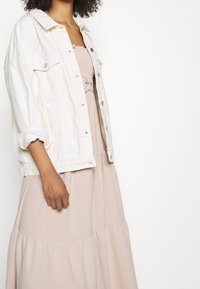 Bílá džínová bunda s vyhrnutými rukávy přes světle růžové vrstvené šaty s nařaseným živůtkem a mašlí v pase.