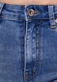 Jeans de mezclilla azul claro con cierre de botón, costuras visibles y un ligero desgaste. Las características incluyen un diseño de bolsillo frontal estándar.