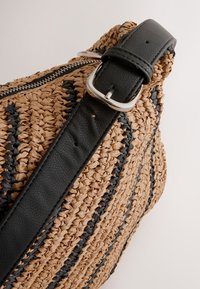 Borsa intrecciata in paglia con strisce blu scuro e marrone naturale, dotata di tracolla in pelle nera e chiusura in metallo argentato.