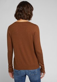 Brązowy sweter z długim rękawem, lekka dzianina, okrągły dekolt, dopasowany krój, z prążkowanymi mankietami, połączony z niebieskimi dżinsami.