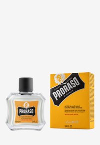 Baume après-rasage Proraso dans un flacon hexagonal transparent avec un capuchon noir, arborant une étiquette orange ; livré dans un emballage avec un design orange assorti.