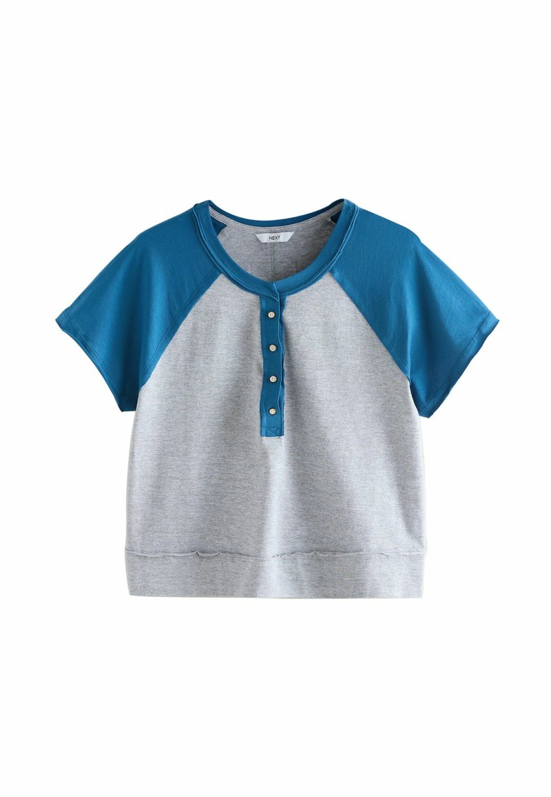Top gris de manga corta con mangas raglán azules y una tapeta de botones. Presenta una textura suave y un corte holgado.