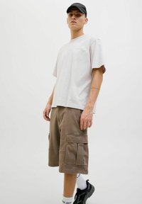 Jasnoszara koszulka typu t-shirt, luźny krój, zestawiona z brązowymi szortami cargo z bocznymi kieszeniami. Uzupełniona czarnymi trampkami i czapką w kolorze czarnym.