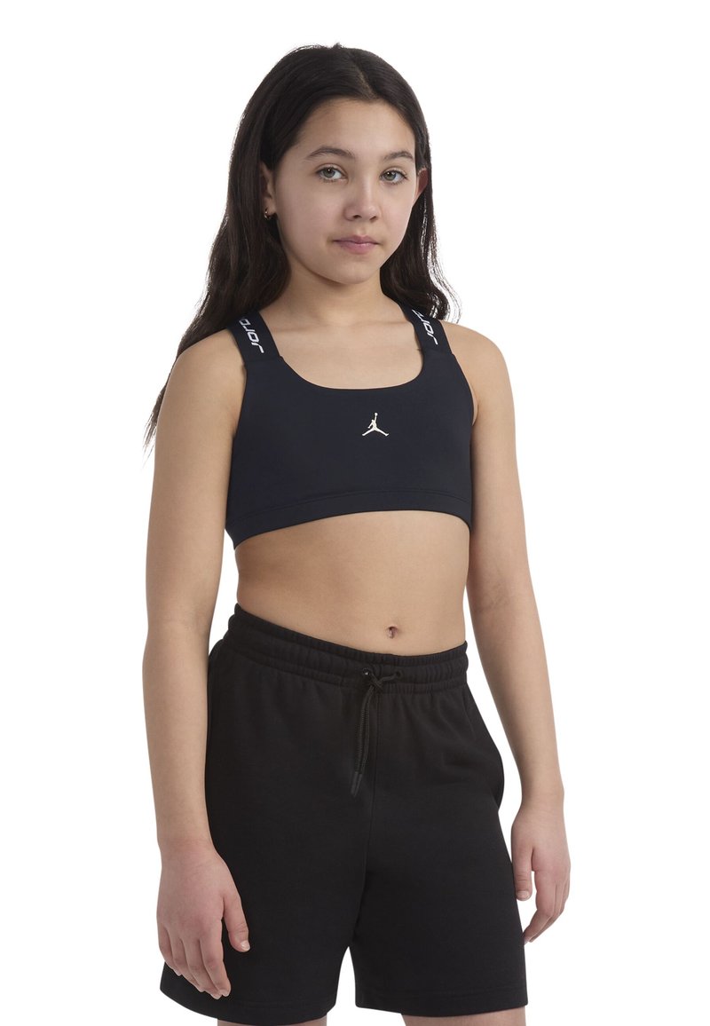 Melnā sporta krūšturis ar Jordan zīmolu, platai siksniņai, uz kuras ir redzams zīmola nosaukums, apvienots ar melniem šortiem ar aukliņu. Gluda, sportiska auduma tekstūra.