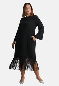 Černé šaty s dlouhými rukávy a třásňovým lemem. Vyrobené z měkkého materiálu, mají boční kapsy a volný střih. Žádné další vzory.