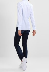 Jasnoniebieska koszula w paski z guzikami z tylnym yoke'm, połączona z ciemnymi dżinsami i białymi sneakersami z czerwonymi akcentami w kształcie gwiazd.