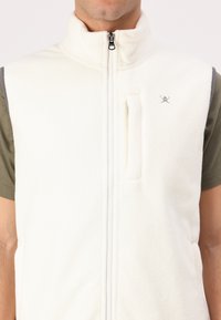 Weißer Fleece-Weste mit hohem Kragen, durchgehendem Reißverschluss und einer Reißverschlusstasche auf der Brust. Mit grauen Akzenten an den Schultern.