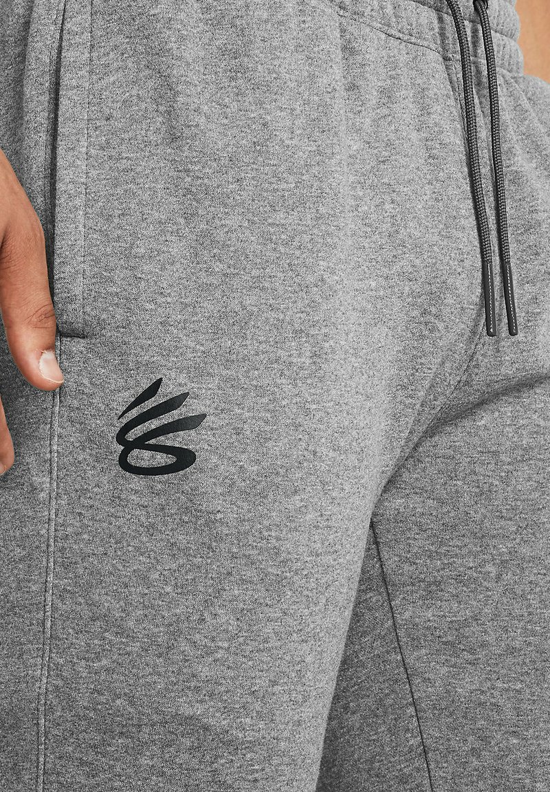 Szare dresy wykonane z miękkiej tkaniny mają elastyczny pas ze sznurkiem i czarny wzór logo na udzie. Tekstura jest gładka i lekko melanżowa.