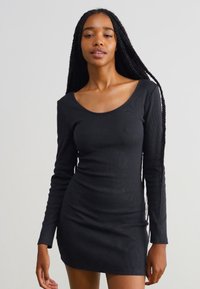 Robe noire à manches longues avec un décolleté en scoop, design ajusté, texture côtelée extensible, arrivant mi-cuisse. Style simple et polyvalent.