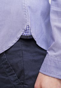 Close-up of a person wearing navy pants and a blue striped shirt with a checkered underlayer visible near the waist.