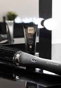 Crème de coiffage volumisante GHD Volume Forever dans un tube noir de 100 ml, à côté d'un sèche-cheveux GHD Duet noir et gris avec un bouton bleu.