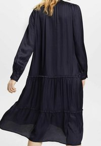 Marinblå, långärmad klänning med en lagerdesign, tillverkad av ett mjukt, flytande tyg. Har volangdetaljer och en lös siluett.