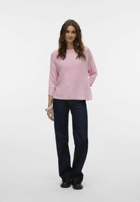 Maglione rosa a coste con una vestibilità ampia e maniche a tre quarti, abbinato a jeans a gamba larga blu scuro e scarpe nere.