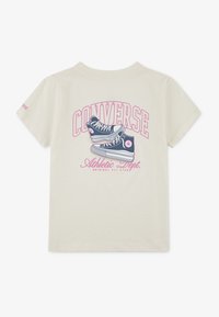 T-shirt en coton couleur crème présentant un graphique de baskets Converse bleues et un texte coloré indiquant "CONVERSE Athletic Dept." au dos.