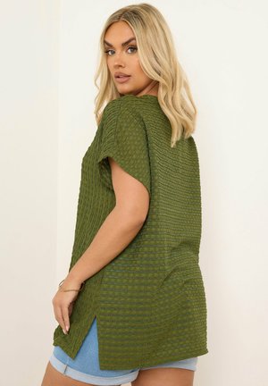 Grøn tekstureret top med korte ærmer, der har et ribbet design og sideslidser, parret med lyseblå denimshorts.