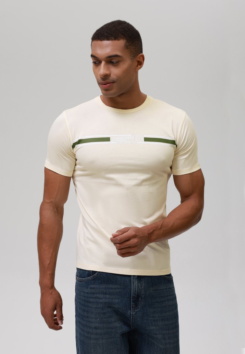 Camiseta de manga corta color crema con un diseño ajustado, que presenta rayas horizontales en verde oscuro y blanco, y una tela texturizada.