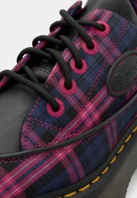 Black sneaker with a pink and blue plaid pattern. Features black laces and eyelets, with a textured sole and logo patch on the side.