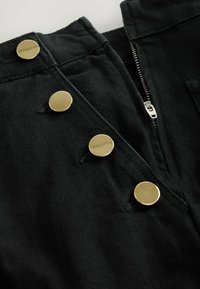 Czarny materiałowy ubranie z zamkiem błyskawicznym i pięcioma błyszczącymi złotymi guzikami. Charakteryzuje się miękką teksturą i uporządkowanym kształtem.