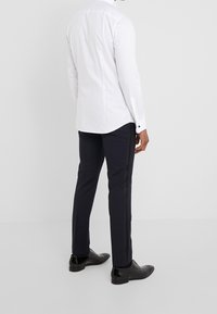 Camicia bianca a maniche lunghe con orlo curvo, abbinata a pantaloni navy con una sottile striscia laterale nera e scarpe nere. Tessura liscia.