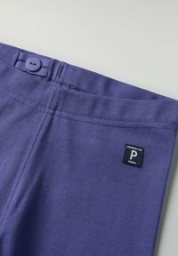 Violetit puuvillahousut, joissa on sileä pinta, napituksessa ja mustassa tarrassa valkoisella tekstillä vyötäröllä.