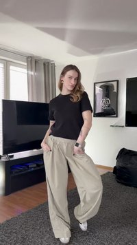 Must lühikeste varrukatega t-särk koos lahtiste beežide pükstega, millel on elastne vöökoht ja suured küljetaskud, kantud valgete tossudega.