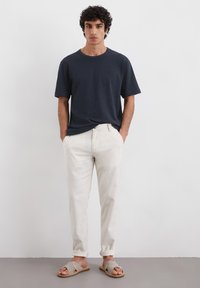 Marineblå bomulds t-shirt parret med lyse beige linnedbukser og grå sandaler. Enkel design med korte ærmer og en afslappet pasform.
