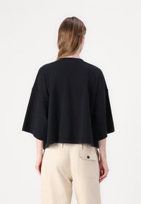 Μαύρο βαμβακερό oversize τοπ με φαρδιές μανίκες και κοντό στρίφωμα, σε συνδυασμό με ανοιχτό μπεζ παντελόνια που διαθέτουν πίσω τσέπη και λεπτομέρεια κουμπιού.