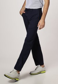 Námořnické modré kalhoty se střihem rovného nohavice, vyrobené z hladké tkaniny. V kombinaci se světlými šedými botami s zeleným akcentem.