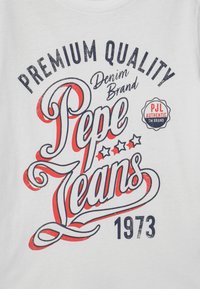 Camiseta blanca con un gráfico impreso colorido que incluye "Marca de Denim de Calidad Premium Pepe Jeans" y "1973", acentuado con estrellas y remolinos.