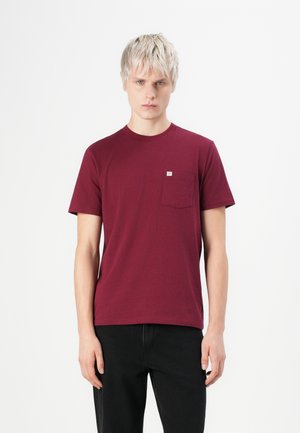 Bordeauxfarbenes T-Shirt aus Baumwollstoff mit Rundhalsausschnitt und kurzen Ärmeln. Verfügt über eine kleine Brusttasche mit Etikett.