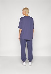 T-shirt en coton violet surdimensionné et jogging assorti, avec une coupe décontractée et des poignets élastiques, associés à des chaussures de sport blanches.