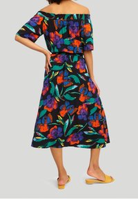 Abito nero off-the-shoulder con stampa floreale colorata in rosso, viola e verde; scollatura elastica; lunghezza midi; abbinato a sandali gialli.