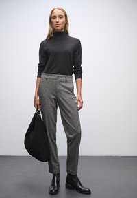 Pull en col roulé noir, pantalon à carreaux gris, bottines noires et un grand sac noir. Textures lisses avec une silhouette ajustée.