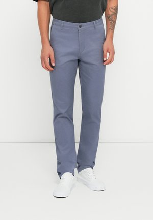 Light blue dress pants made of twill fabric, featuring a button closure, straight fit, and pockets. Paired with white sneakers.