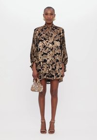 Rochie neagră cu imprimeu paisley aurie, mâneci lungi și guler înalt. Combinată cu o geantă mini florală și sandale cu barete nude.
