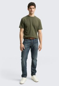 Oliwkowozielona bawełniana koszulka w połączeniu z niebieskimi dżinsami i białymi trampkami. Charakteryzuje się klasycznym okrągłym dekoltem i luźnym krojem.